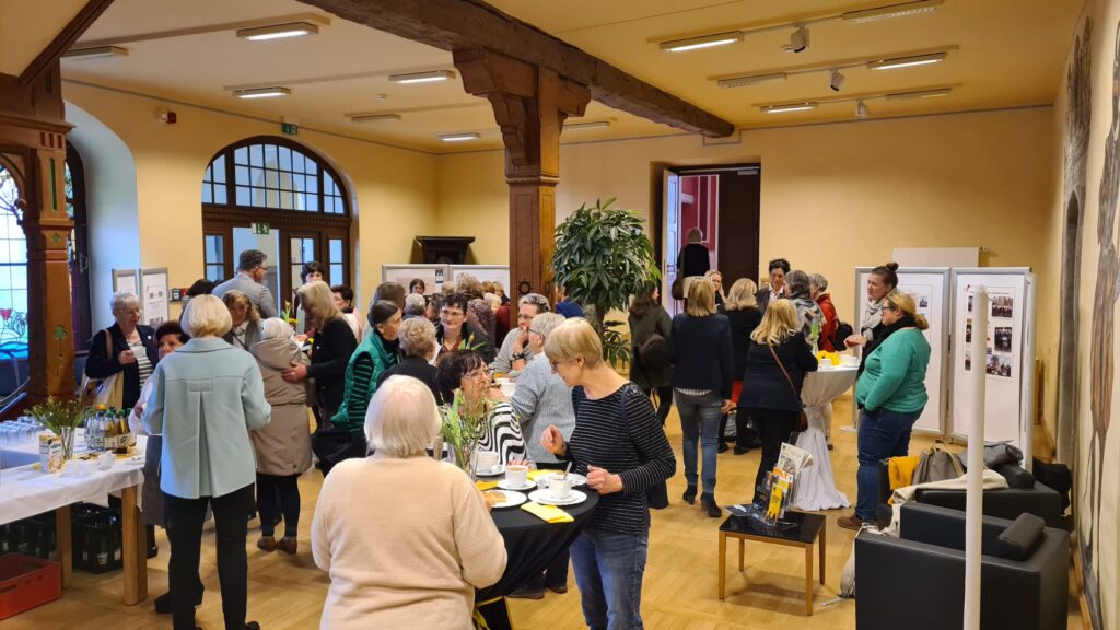 Viele Frauen, die an Stehtischen Kaffee trinken und Kuchen essen